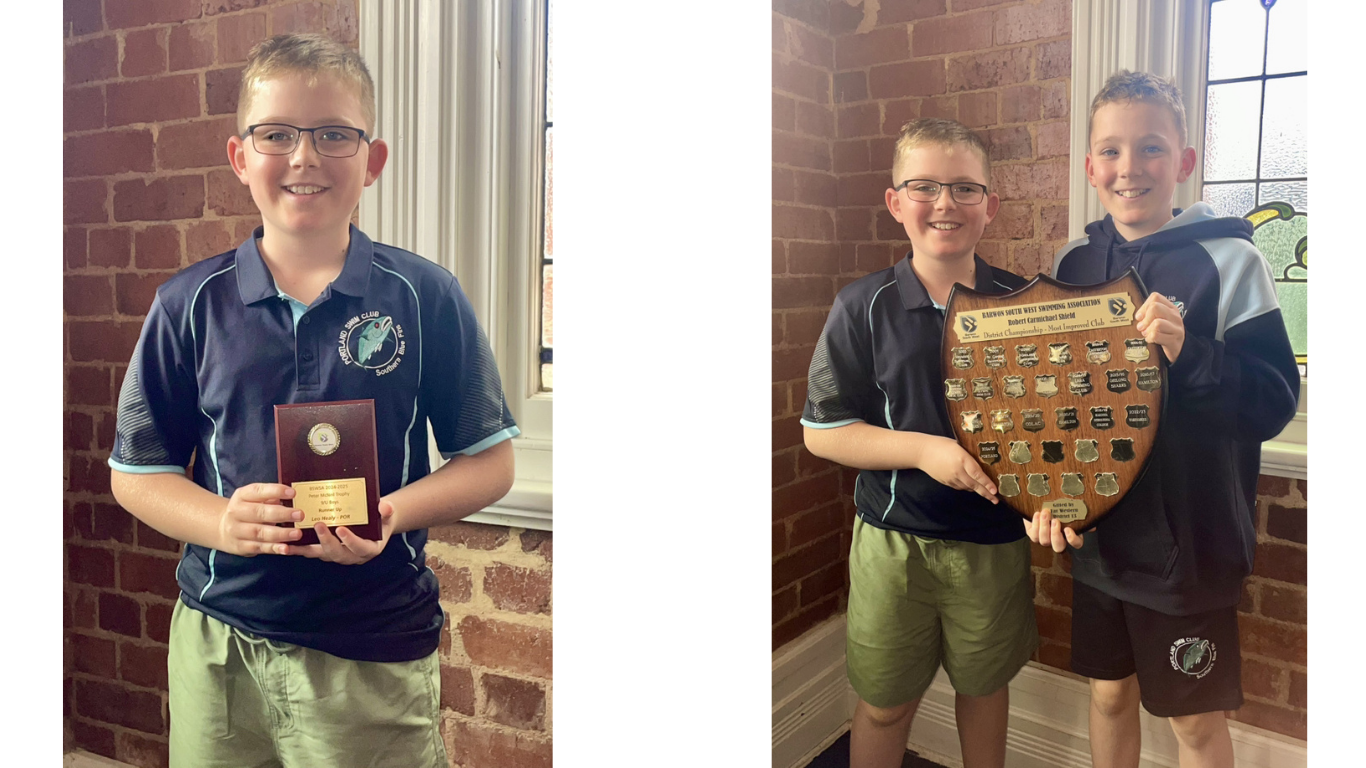 Boy with blue shirt holding timber trophy with gold plaque to left. Two boys holding timber shield award to right